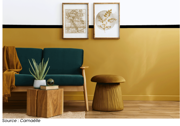 Salon moderne avec mur peint en jaune, canapé vert, tabouret assorti et décorations murales, par Camaëlle.