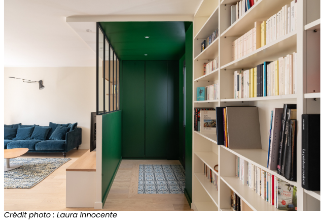 Intérieur moderne avec bibliothèque intégrée, salon avec canapé bleu, et couloir peint en vert, photographié par Laura Innocente.