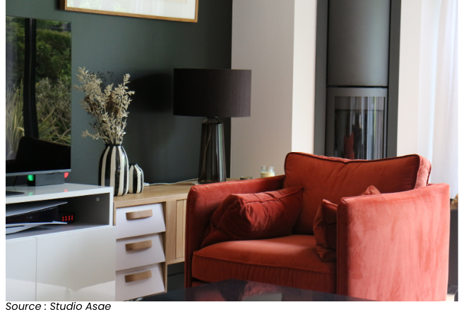 Salon moderne aménagé avec un mur peint en noir par Studio Asae, mettant en valeur un fauteuil rouge et une lampe noire.