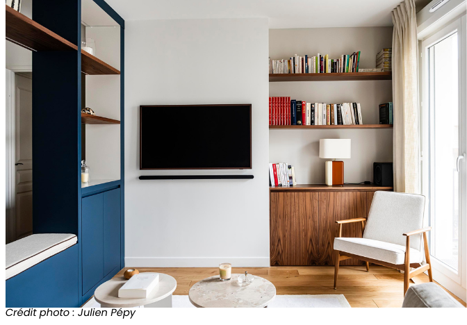 Salon contemporain avec étagères en bois, mur blanc, bibliothèque intégrée, et accents bleus, photographié par Julien Pépy.